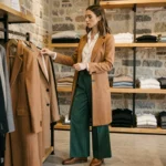 Femme élégante en manteau camel parcourant les rayons d'une boutique de mode parisienne aux murs en pierre